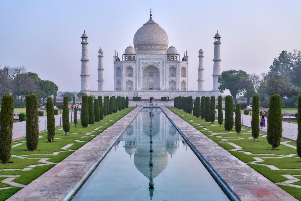 Symmetrical view of the white marble Taj Mahal in Agra reflecting in the long central garden pool lined with manicured cypress trees.