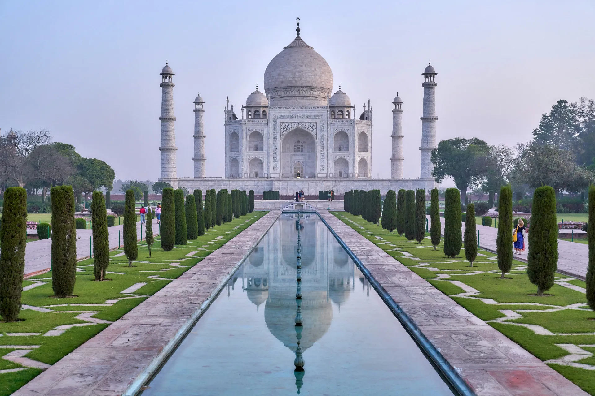 Symmetrical view of the white marble Taj Mahal in Agra reflecting in the long central garden pool lined with manicured cypress trees.